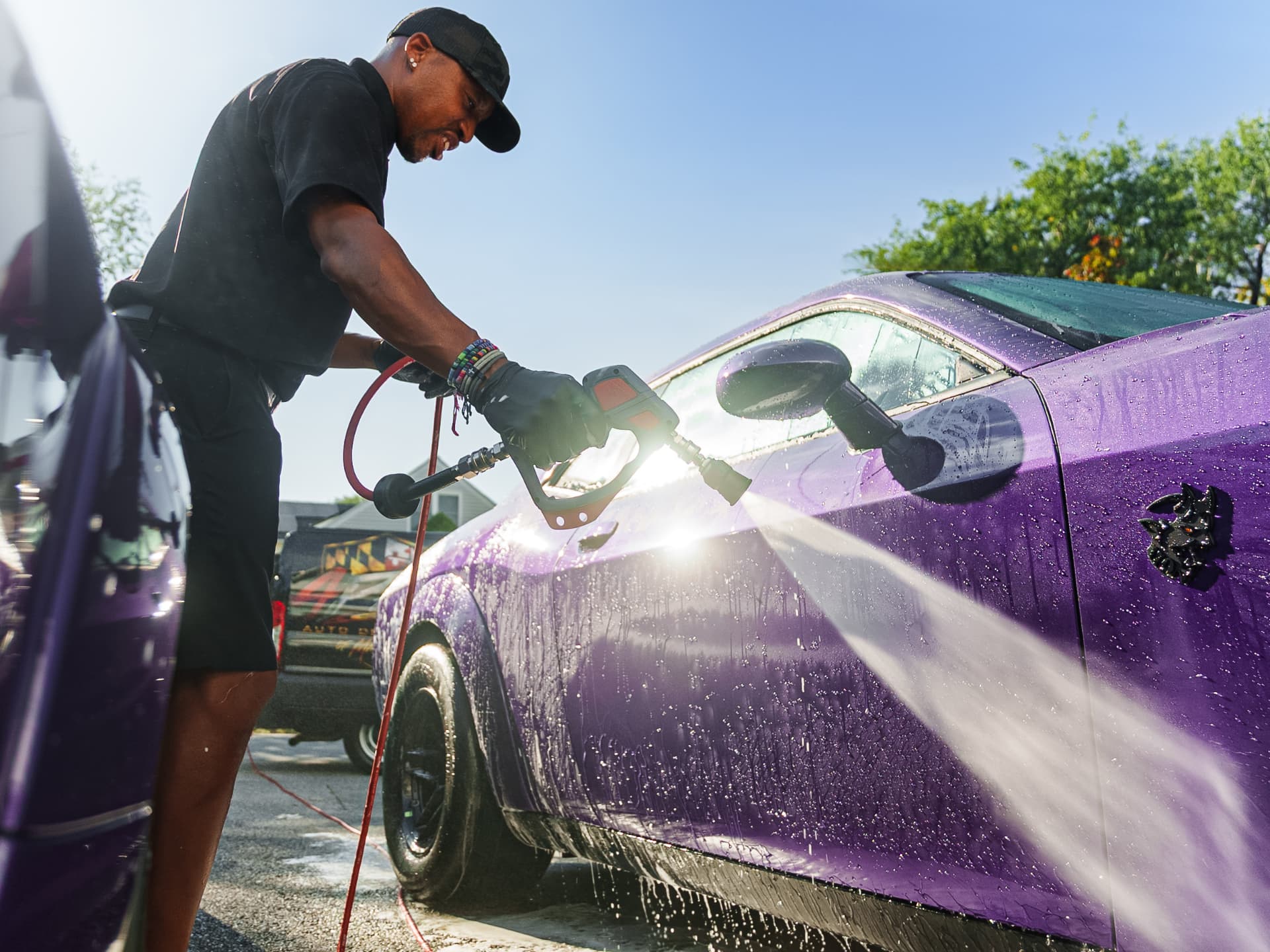 Apex detailer rinsing foam off a purple car during a mobile detail