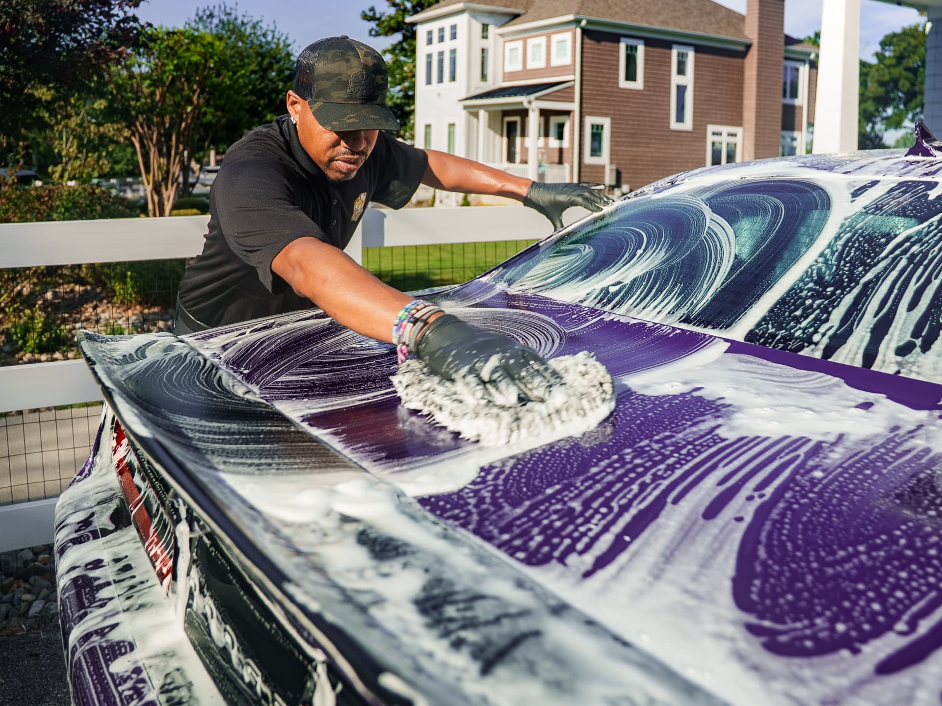 Apex detailer hand washing a purple car with a foam mitt in the driveway